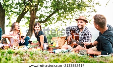 Friends group having fun moment at pic nic playing guitar on sunset - Friendship life style concept with young people enjoying springtime camping together at park location - Bright greenish filter