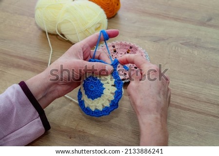 Woman and her fingers knitting flower-patterned coasters from blue crochet and blue and white threads on a wooden table. hand creativity.