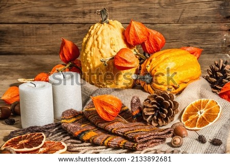 Autumn cozy composition. Scarf, warm mittens, candles, pumpkins, fall decor. Wooden rustic background