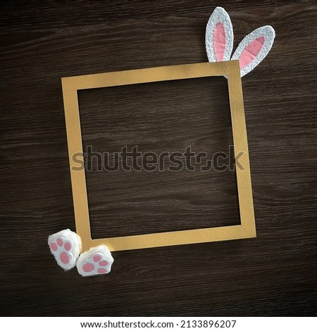 Golden square frame and bunny ears and paws on a wooden background. Text space. Top view. Flat lay. Holiday, Easter.