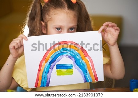 No war. Little sad girl draws a picture about Ukraine. Draws a rainbow and the Ukrainian flag