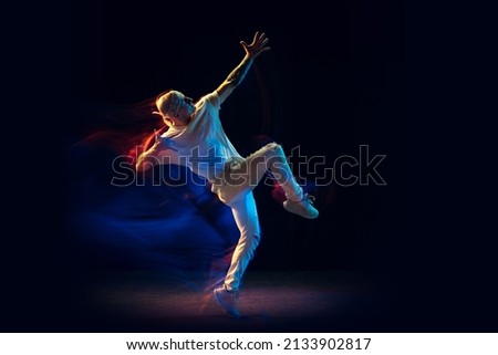Hip-hop moves. Bald man in white jeans and tee dancing hip-hop isolated on dark background in mixed neon light. Youth culture, modern dances, movement, style and fashion, action.
