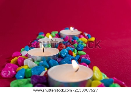 Small white candles on multi-colored stones and red background. spa concept