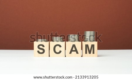 scam text on wooden blocks with coins on brown background, concept