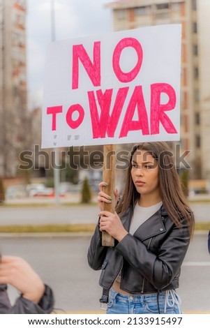 Beautiful and young girl is holding the protest sign outisde on the street while being sad