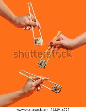 Women's hands hold sushi rolls with sticks. Orange background. Creative concept