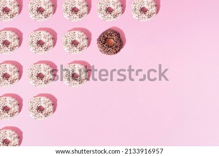 Arranged ring donuts like a triangle with white and chocolate glaze. Colorful crumbs on a pink pastel background. Copy space and pattern. Flat lay.