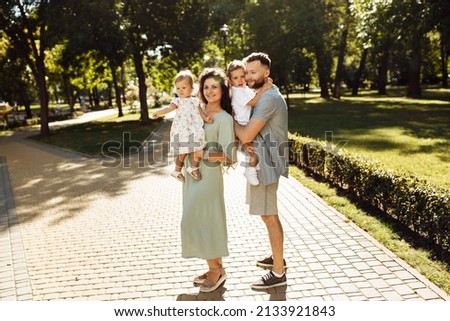 Happy parents with little kids at the park, caring dad hold in arms adorable daughter, beautiful mom hold joyful son, loving husband gentle kiss lovely wife, family concept. High quality photo