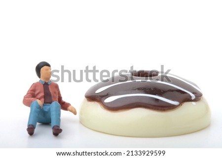 miniature figurine of a man sitting near by a chocolate donut