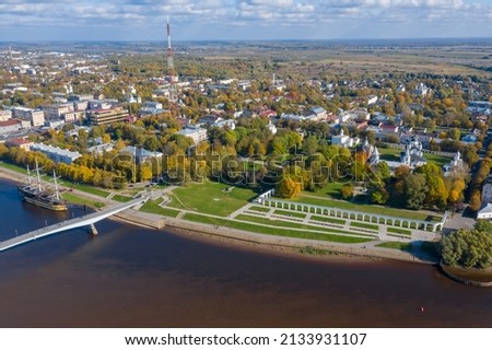 Panoramic aerial view of the Gostiny Dvor Arcade in Veliky Novgorod, autumn treetops on a sunny day. Remaining ruins of a medieval market. Great bridge over the Volkhov river.