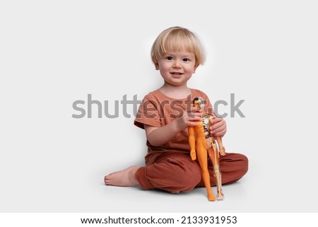 little boy holding a toy, human model for studying anatomy, body structure, location of internal organs, biology, preschool education, child development, study of body parts, skeleton, heart, lungs Royalty-Free Stock Photo #2133931953