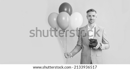 happy mature man with box and party balloons on yellow background, copy space, mens day