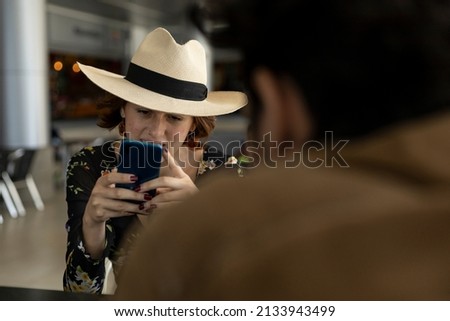 Young Latin American girl (22) with cowboy hat is sending a message from her cell phone. Concept of technology.