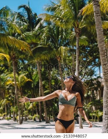 Female model posing in a bikini on a paradise beach with palm trees
