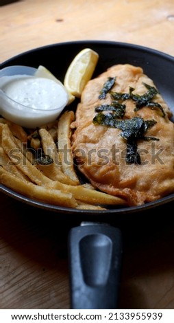 close up fish and chips in a black frying pan
