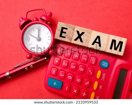 Top view calculator,pen and clock with text EXAM on red background.