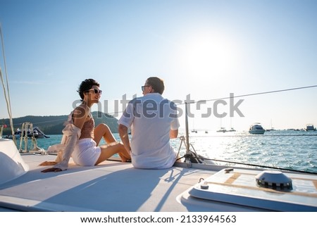 Caucasian man and woman couple enjoy outdoor luxury party drinking champagne with talking together while catamaran boat sailing. Male and female relax with outdoor lifestyle on summer travel vacation Royalty-Free Stock Photo #2133964563
