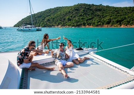 Group of man and woman friends enjoy party drinking champagne with talking together while catamaran boat sailing at summer sunset. Male and female relax outdoor lifestyle on tropical travel vacation Royalty-Free Stock Photo #2133964581