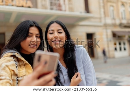 Two young and cheerful Latin women take a picture with their mobile phone while tourism in a city during a trip. sisters having a good time together