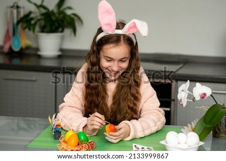 A girls in hare ears paints eggs. Easter. She is at home in the kitchen. Preparation for the holiday.