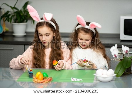 Two girls in hare ears paint eggs. Easter. They are at home in the kitchen. Preparation for the holiday.