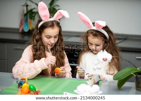 Two girls in hare ears paint eggs. Easter. They are at home in the kitchen. Preparation for the holiday.