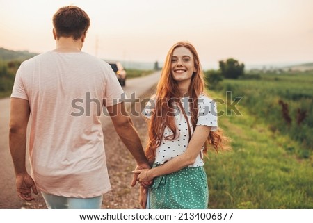 Man and woman walking on the side of the road holding hands, woman turning her face to the camera, smiling. Beautiful young girl. Summer vacation. Pretty young Royalty-Free Stock Photo #2134006877