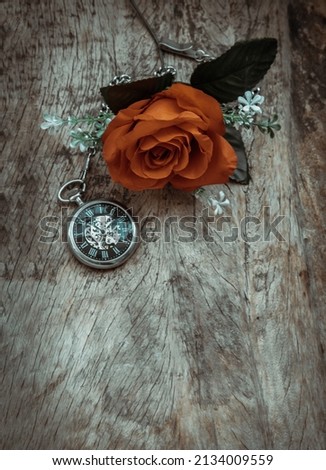 Orange rose flower and A retro pocket watch on old wooden board background. Copy space, No focus, specifically.