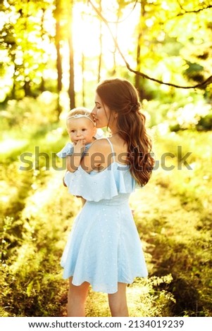Tender woman holds little baby girl in arms, walking at the park, hugging, lovely mother kissing adorable daughter, enjoy family moments, weekend outdoors, parenthood concept. High quality photo