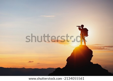 vision for success ideas. businessman's perspective for future planning. Silhouette of man holding binoculars on mountain peak against bright sunlight sky background. Royalty-Free Stock Photo #2134055561