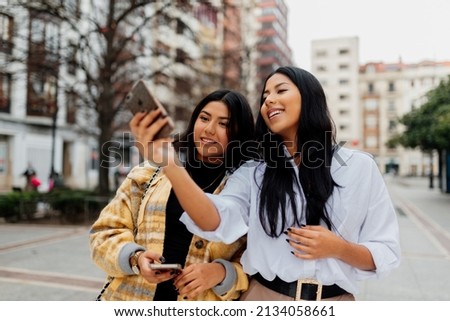 Two young and cheerful Latin women take a picture with their mobile phone while tourism in a city during a trip. sisters having a good time together