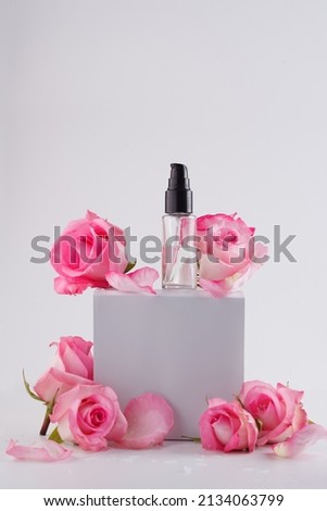 Bottle of facial serum on stone with rose flower on gray background, copy space