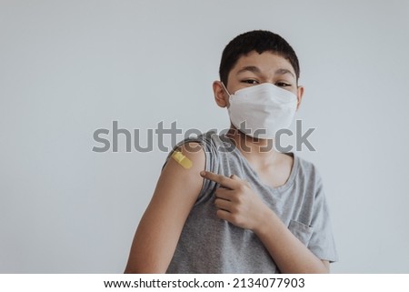 Asian boy showing shoulders after getting a vaccine. Happy little boy showing arm with band-aids on after vaccine injection. Royalty-Free Stock Photo #2134077903