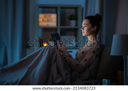 technology, bedtime and people concept - teenage girl with tablet pc computer and earphones sitting in bed at home at night