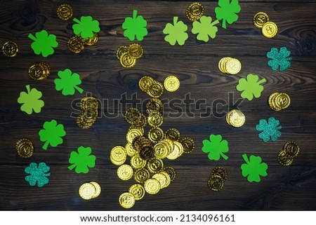 On a dark wooden table there are coins and a four-leaf clover for St. Patrick's Day