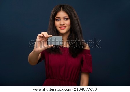 Young smiling beautiful girl posing with a credit or debit card on grey background.
