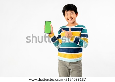 Young Asian Kid holding a phone in his hands with a green screen standing on a white isolated background with copy space.