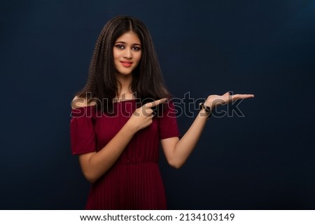 Portrait of beautiful young girl presenting something, showing copy space on her palm on a grey background