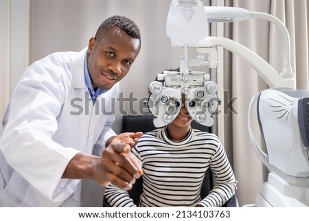 African young woman girl doing eye test checking examination with male man optometrist using phoropter in clinic or optical shop. Eyecare concept. Royalty-Free Stock Photo #2134103763
