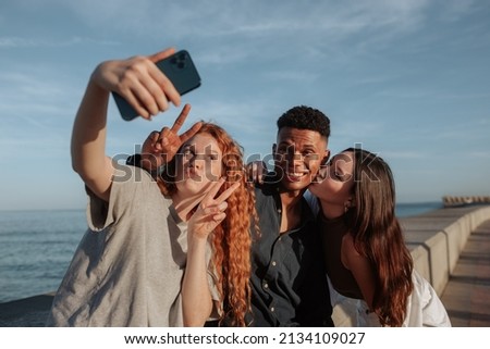 Young friends taking a group selfie next to the sea. Group of carefree friends posing for the camera phone while hanging out together on the weekend. Three friends making memories together.