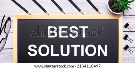 On a light wooden table - a board with the text BEST SOLUTION, pencils, plants, glasses and paper clips. Business concept