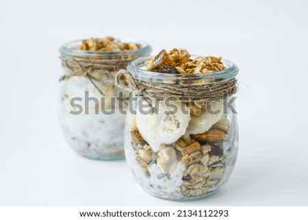 Healthy breakfast. Oatmeal Granola with greek yogurt and nuts banana muesli in jars on light background. Vegan, vegetarian and weight loss diet concept. Detox menu.