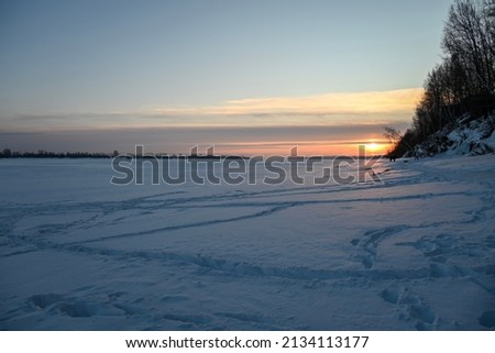 a frozen river with banks stretching towards the horizon. Photo taken at dusk with sun rays and clouds
