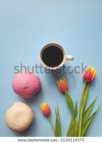Morning with cup of hot coffee and sweet donuts on blue background. Bouquet of tulips. Top view, copy space, mockup. Flat lay. Food and drinks. Spring holidays. 
