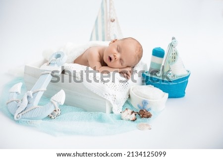 Two week old newborn baby boy wearing a white and blue sailor hat. He is sleeping on his stomach in a tiny sailboat. Sleeping newborn boy on a white background. Photoshoot for the newborn. A portrait  Royalty-Free Stock Photo #2134125099