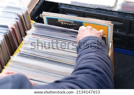 flea market flip in the city, man choosing vinyl records, antiques, old furniture, tables, used things, clothes and other goods are sold on street, recycling of unwanted items, pollution of nature Royalty-Free Stock Photo #2134147653