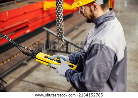 A metal industry worker pressing button on console and operating machine in factory.