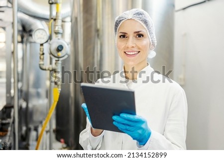 A female milk plant supervisor scrolling on tablet and smiling at the camera. Royalty-Free Stock Photo #2134152899