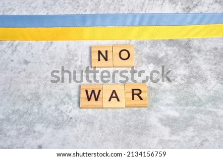 phrase no war is laid out of wooden squares on a gray background with flag of ukraine with blue and yellow ribbon. Concept of peace, war in Ukraine