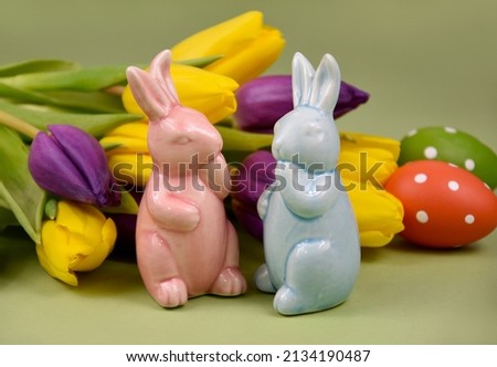 Two cute easter bunnies figurines stock images. Blue and pink easter bunny with tulips and eggs spring decoration still life stock photo